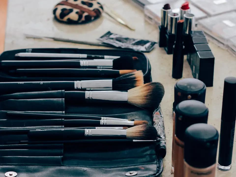 Kuas makeup, lipstik, dan botol alas bedak di meja rias