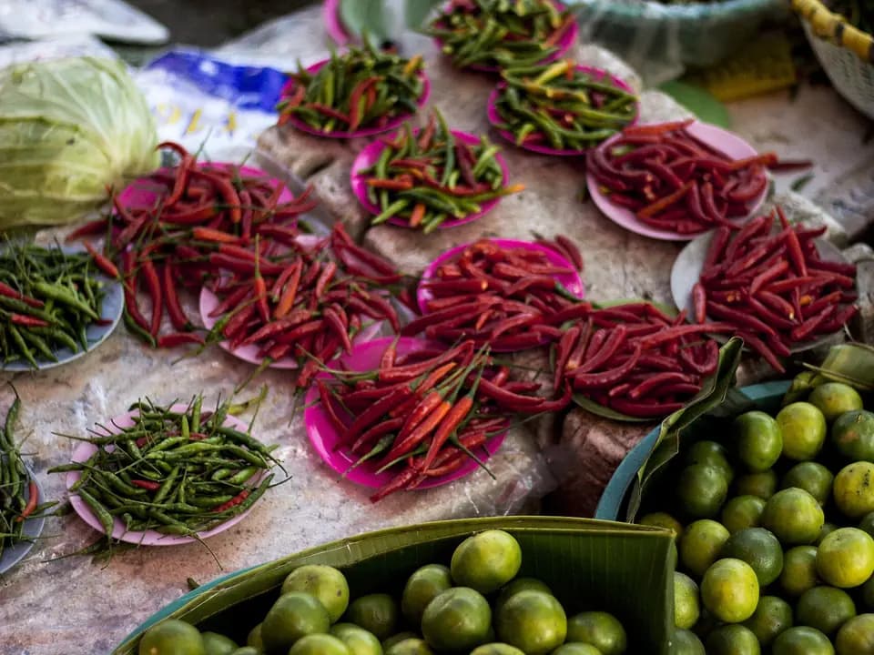 Cabai merah dan hijau di piring, kol, dan jeruk nipis di lapak pasar